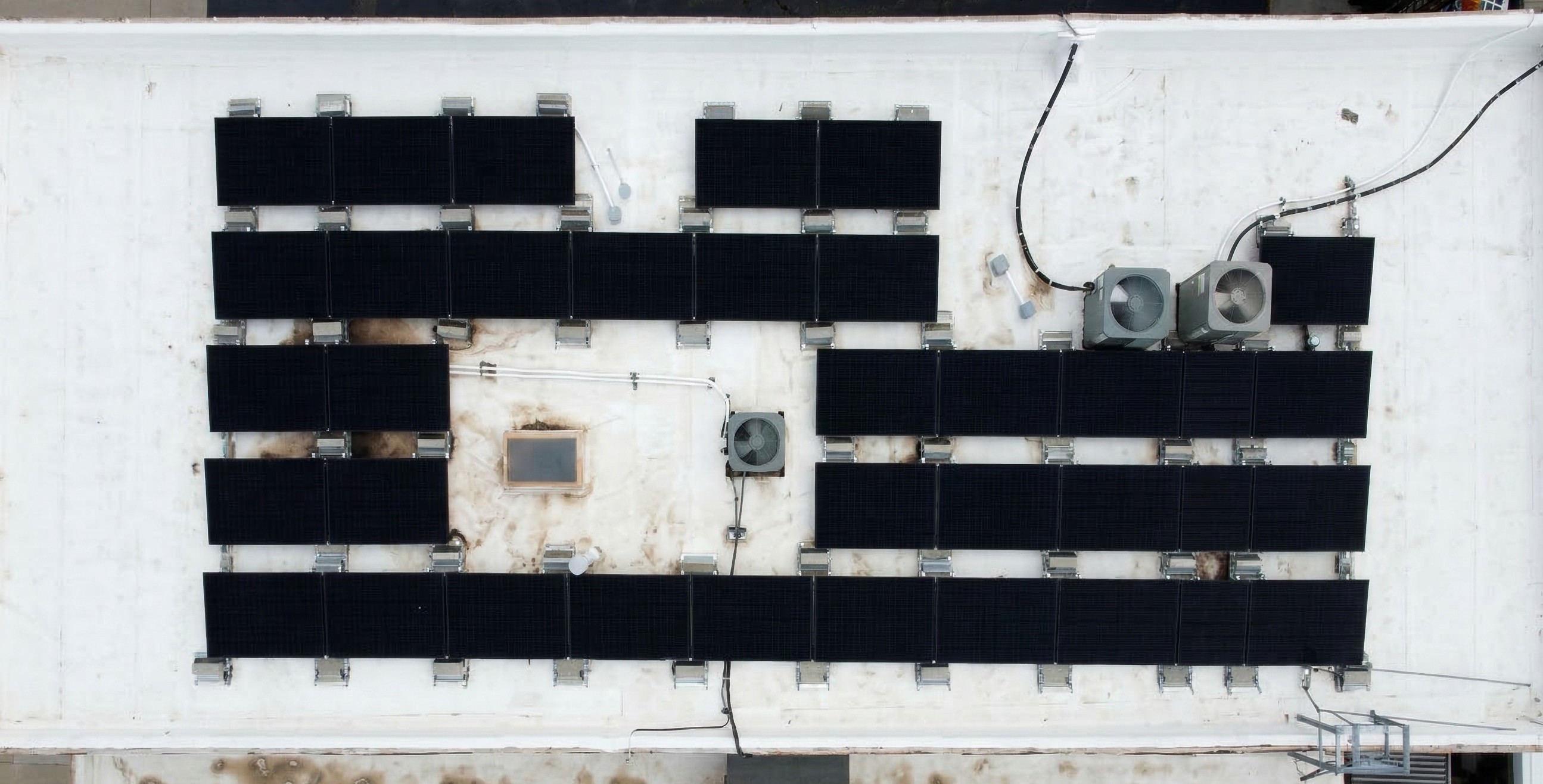 Aerial view of commercial flat roof solar installation with panels arranged around HVAC equipment